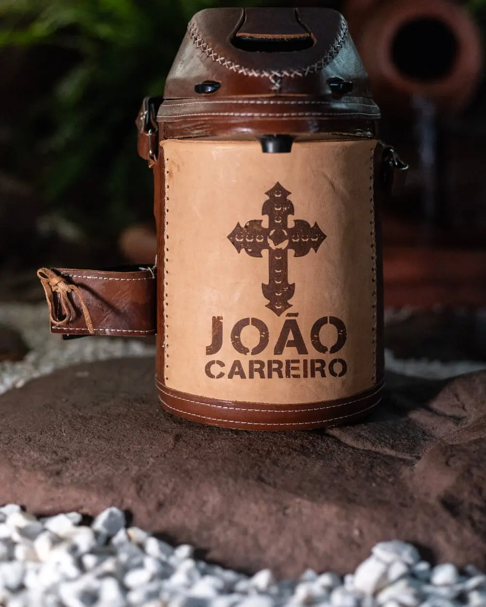 Kit de tereré revestido em couro natural, com a cruz e o nome João Carreiro gravados a fogo, sobre mesa de madeira escura